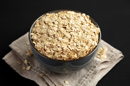 Wholegrain Oat Flakes in a Bowl on a black background, side view, a Food & Drink Photo by LiudmylaChuhunova