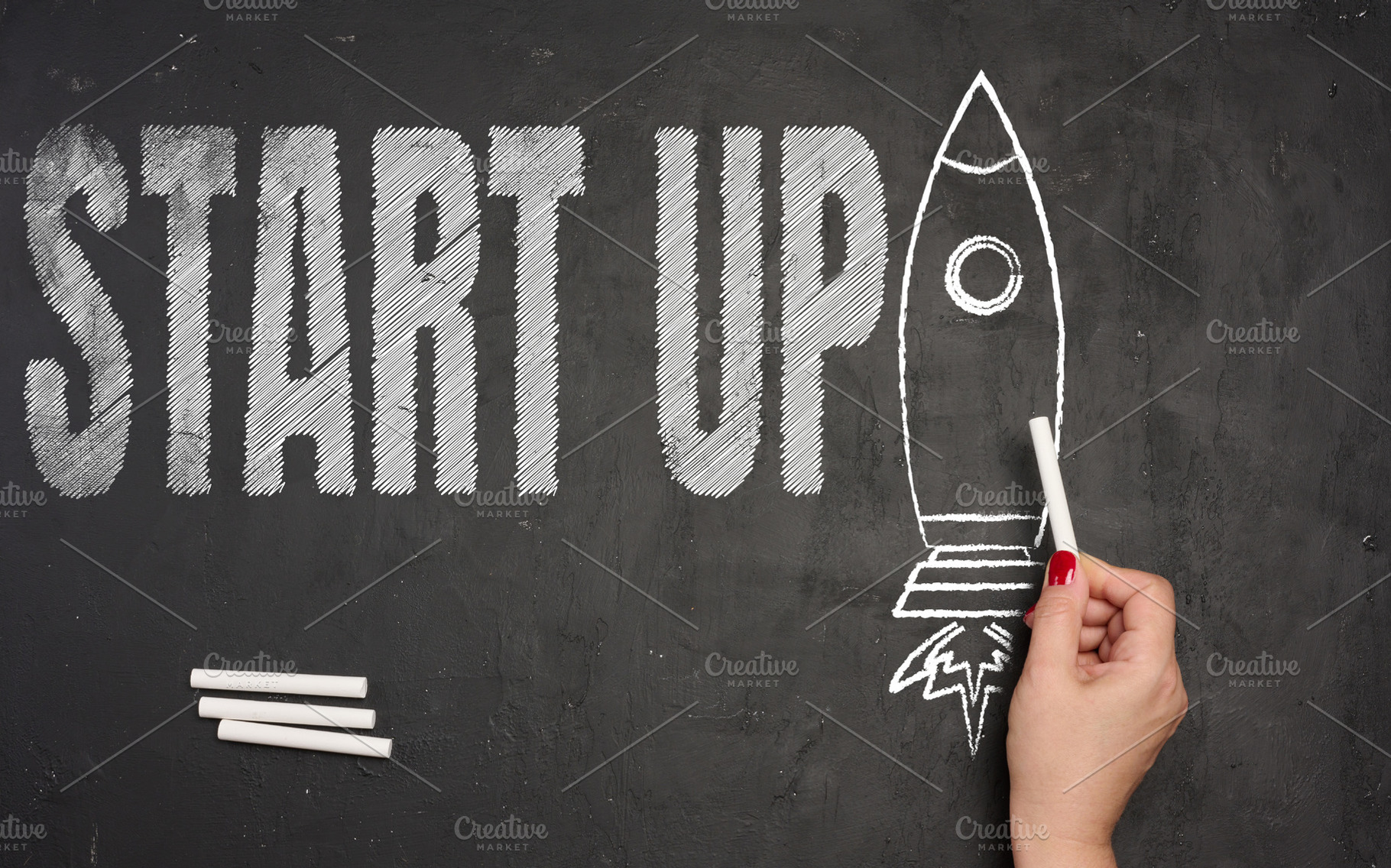 A hand draws the outline of a rocket taking off with white chalk, a Business Photo by ndanko