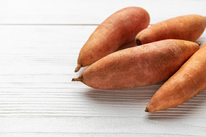 Sweet potato tubers on a light wooden background, a Food & Drink Photo by Olena Rudo