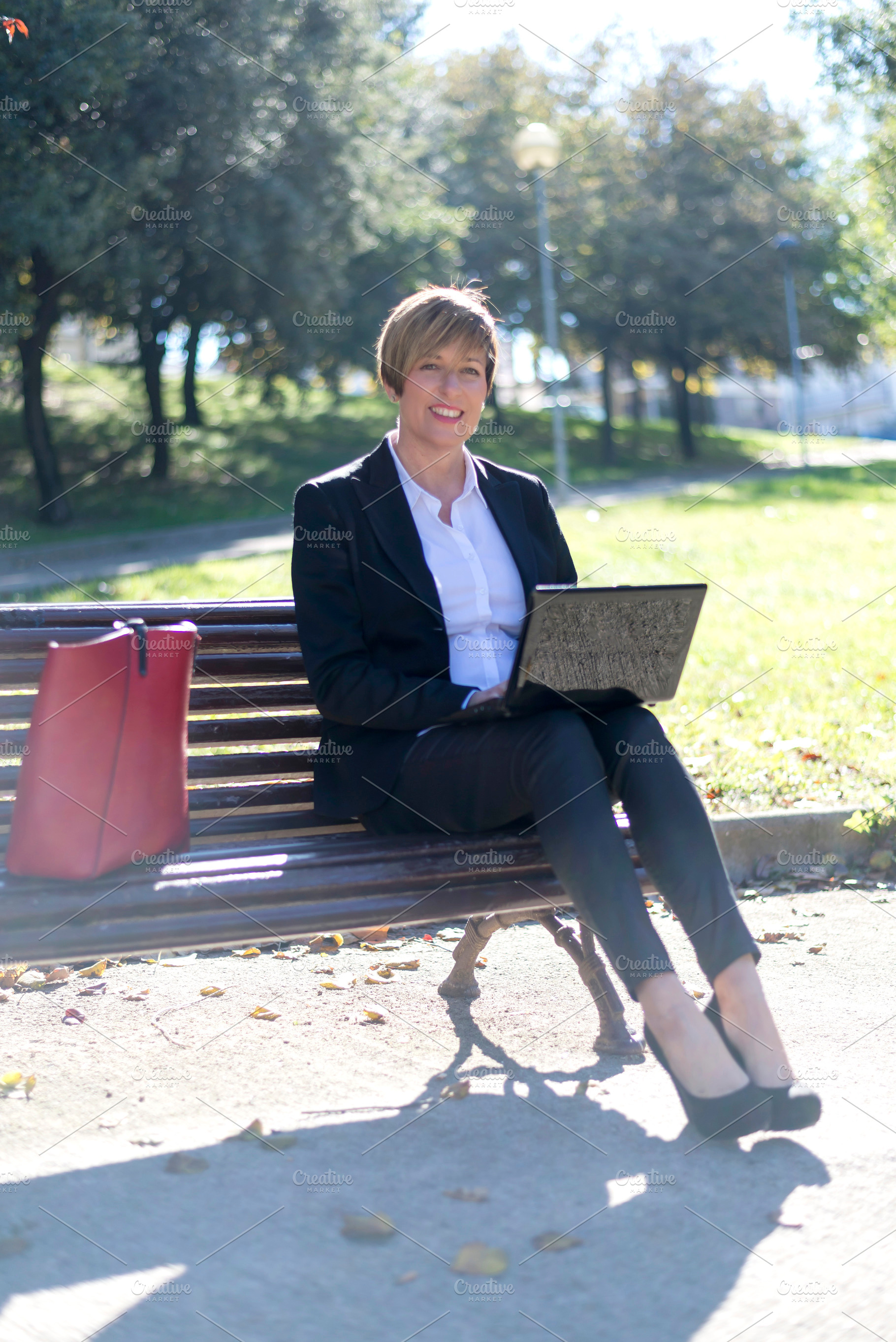 Businesswoman working on laptop in sunny park, a Photo by RF Images
