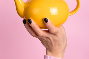 Hand holding a vibrant yellow teapot against a pastel pink backg, a Nature Photo by Ales Munt