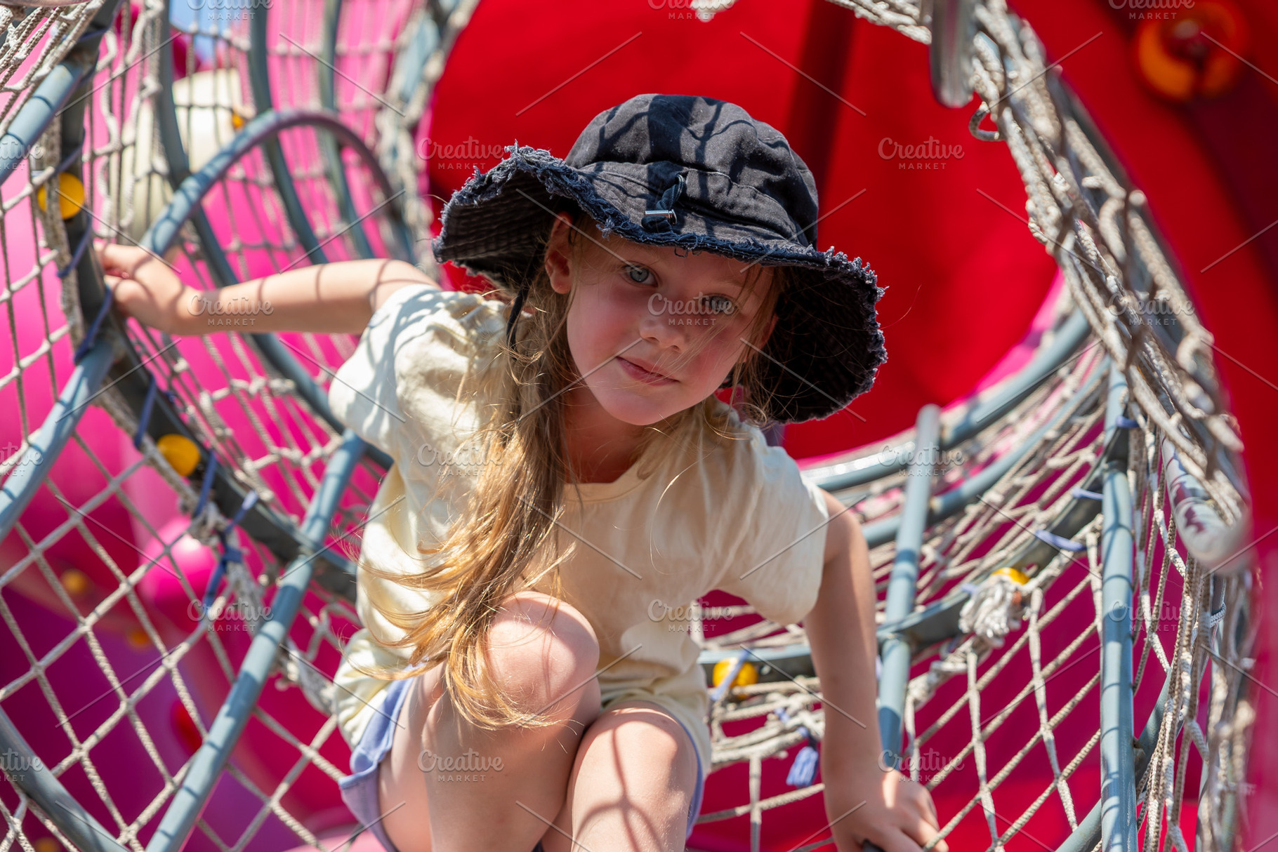 Young girl in sun hat crawling through a net tunnel on a colorful playground, e, a Person Photo by Ales Munt