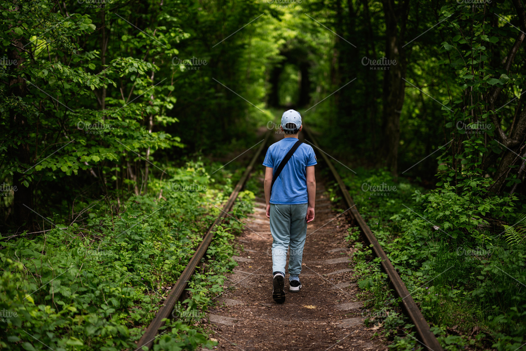 Person walking along a green forest railway track surrounded by nature, a Photo by AS photostudio
