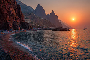 Sunset over beach and dramatic cliff, a Photo by Pixeness Studio