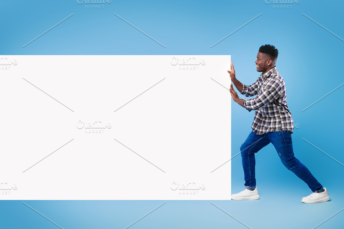 Amazing promo. Handsome young black guy pushing blank white banner with copy sp, a Photo by Prostock-Studio (Photo 2 of 2)