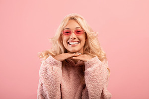 Joyful pretty lady leaning chin on hands and smiling at camera, posing over pin, a Photo by Prostock-Studio