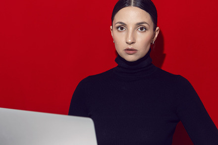 portrait of a brunette woman sitting at a laptop desk on a red background., a Person Photo by SaulichPhoto