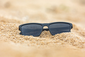 Close-up of black sunglasses partially buried in soft beach sand, capturing a r, a Holiday Photo by Ales Munt