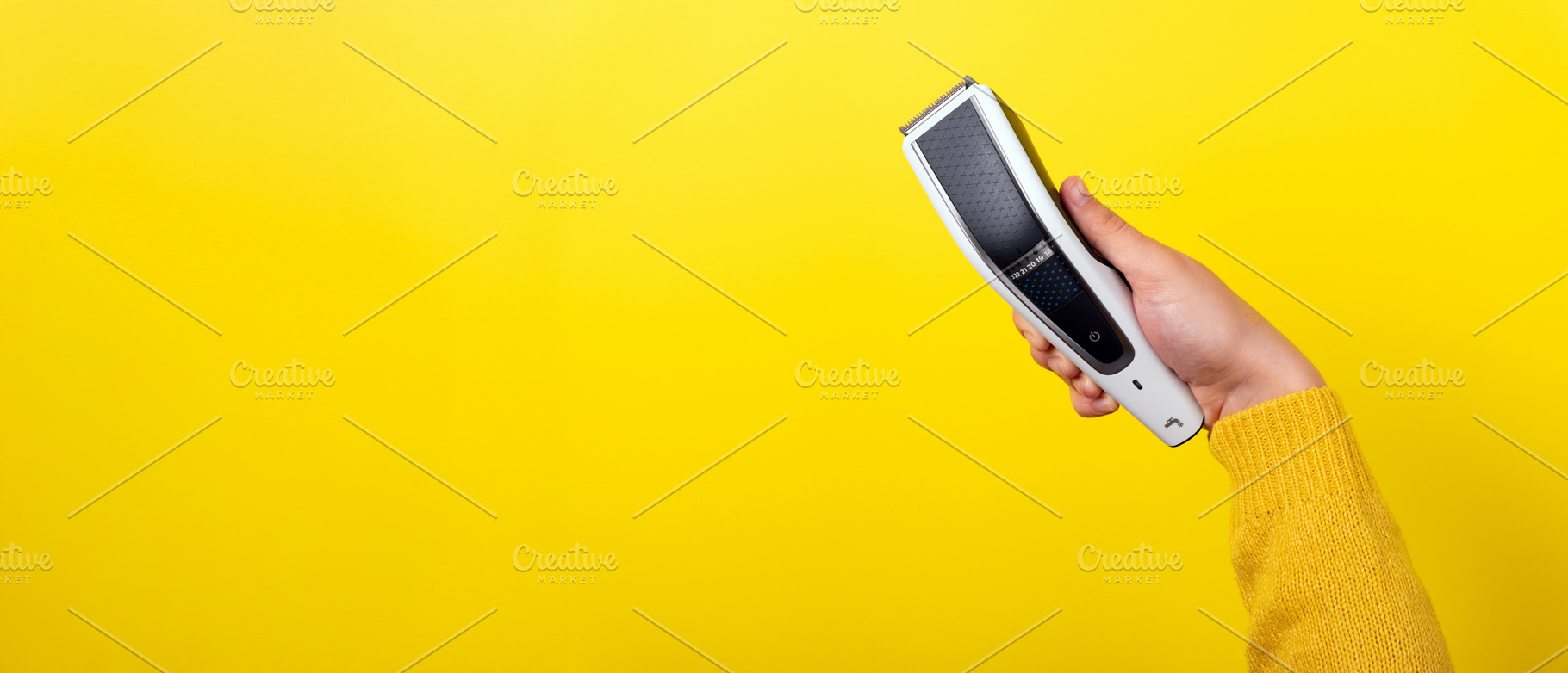 Hand holding an electric hair trimmer against vibrant yellow bac, a Beauty & Fashion Photo by Ales Munt