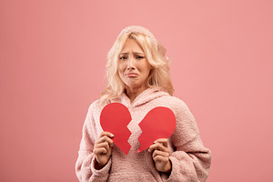Unhappy lady holding two halves of cut paper heart and crying, feeling hurt, go, a Photo by Prostock-Studio