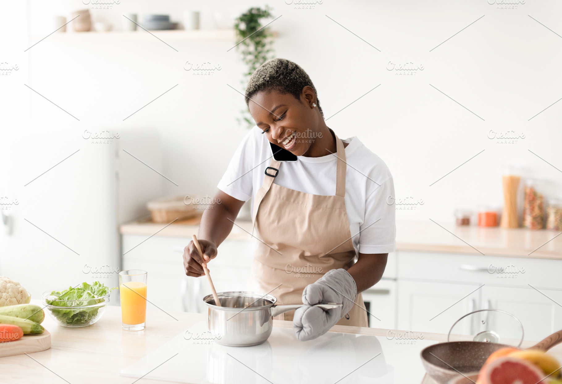 Happy young african american lady in apron prepare food, talk by phone communic, a Person Photo by Prostock-Studio