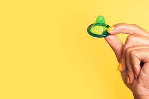 Hand with yellow-painted nails holding a green lubricated condom, a Health & Medical Photo by Ales Munt