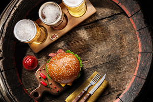 Three glasses of lager beer and hamburger on old wooden barrel., a Food & Drink Photo by Volff