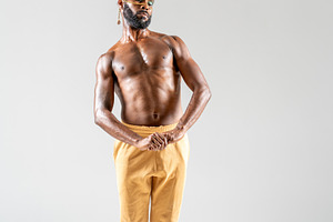 Shy black shirtless gay model holding hand while posing in gray studio, a Person Photo by andreonegin market