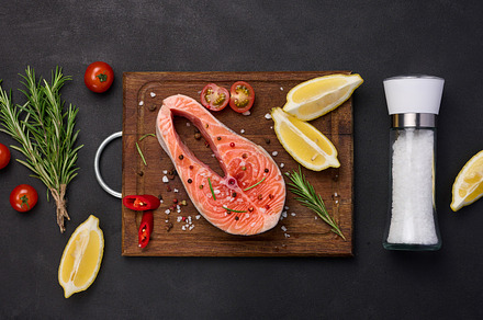 Raw salmon steak on a wooden cutting board, lemon slices, spices, a Food & Drink Photo by ndanko