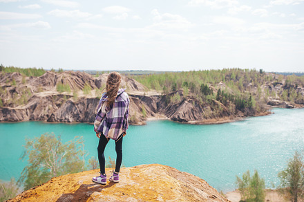 Beautiful girl on the top of the rock with blue lake on background, a Person Photo by travnikovstudio