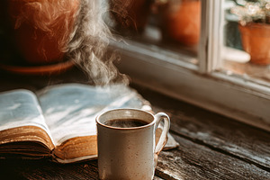 Steaming coffee mug beside open book, a Photo by Pixeness Studio