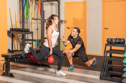 Woman doing lunges with a kettlebell with help of coach with one leg resting on, a Sports & Recreation Photo by Iván Moreno STOCK PHOTO