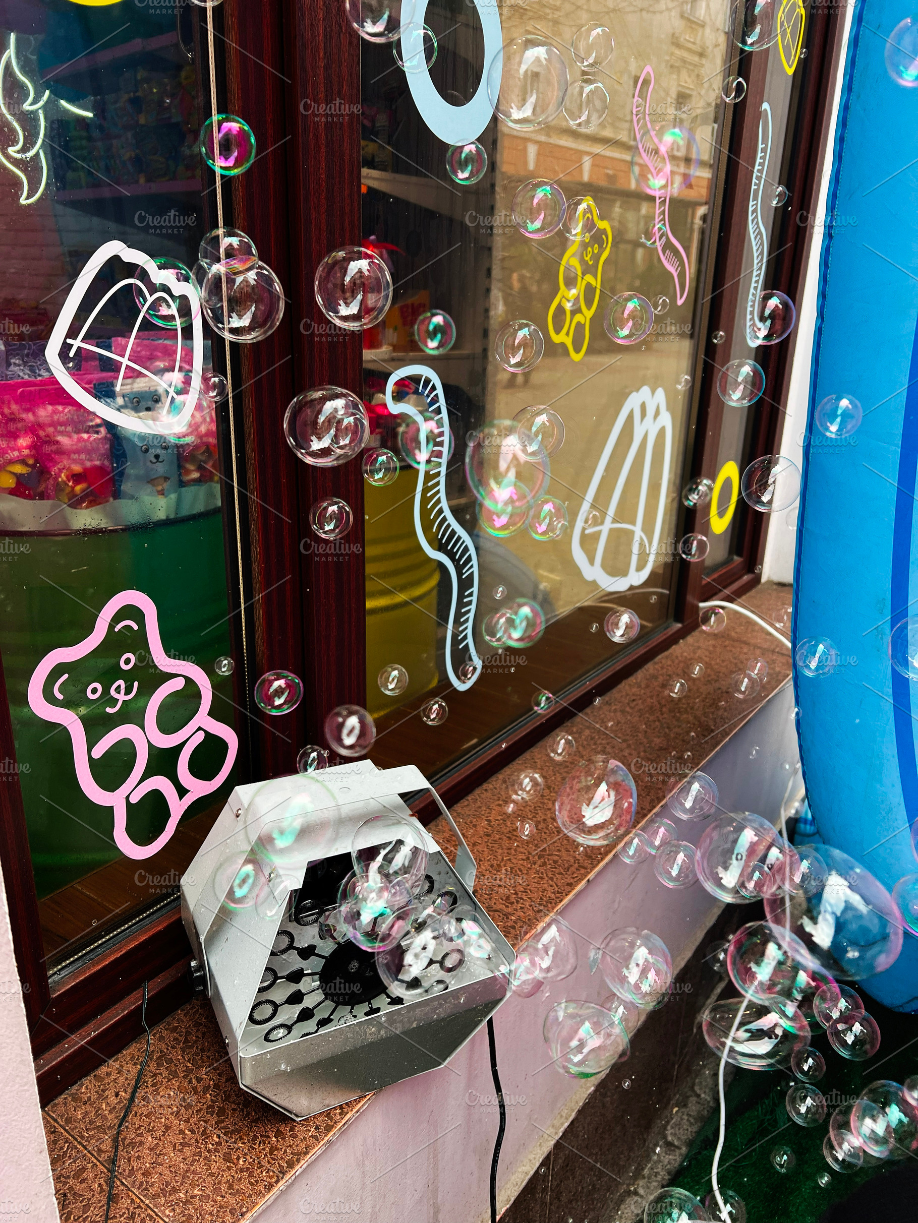 Foam bubble machine producing decorative bubbles outside a colorful storefront, a Photo by AS photostudio