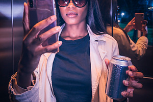 Woman on an elevator taking a selfie and holding a metallic soda, a Person Photo by DanFLCreativo