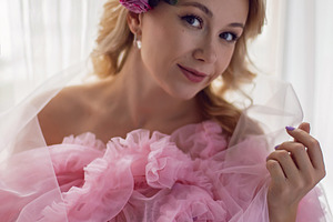 portrait of a fashionable blonde woman in a pink dress and rose flower in her h