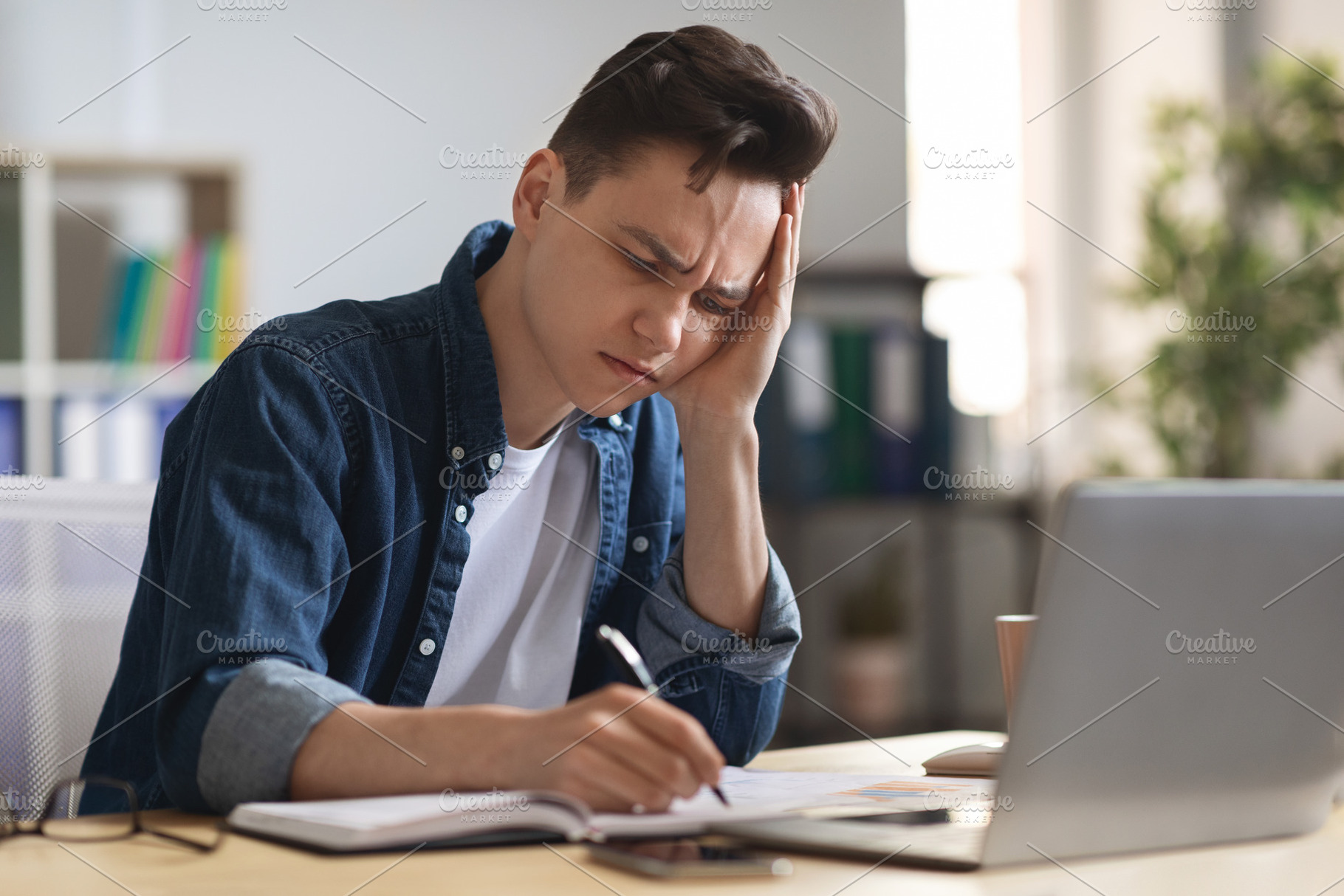 Young male entrepreneur massaging temple, suffering headache at workplace in of, a Photo by Prostock-Studio