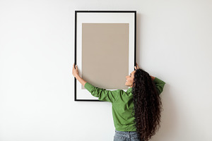 Woman Hanging Frame With Empty Poster On White Wall Indoors, a Photo by Prostock-Studio