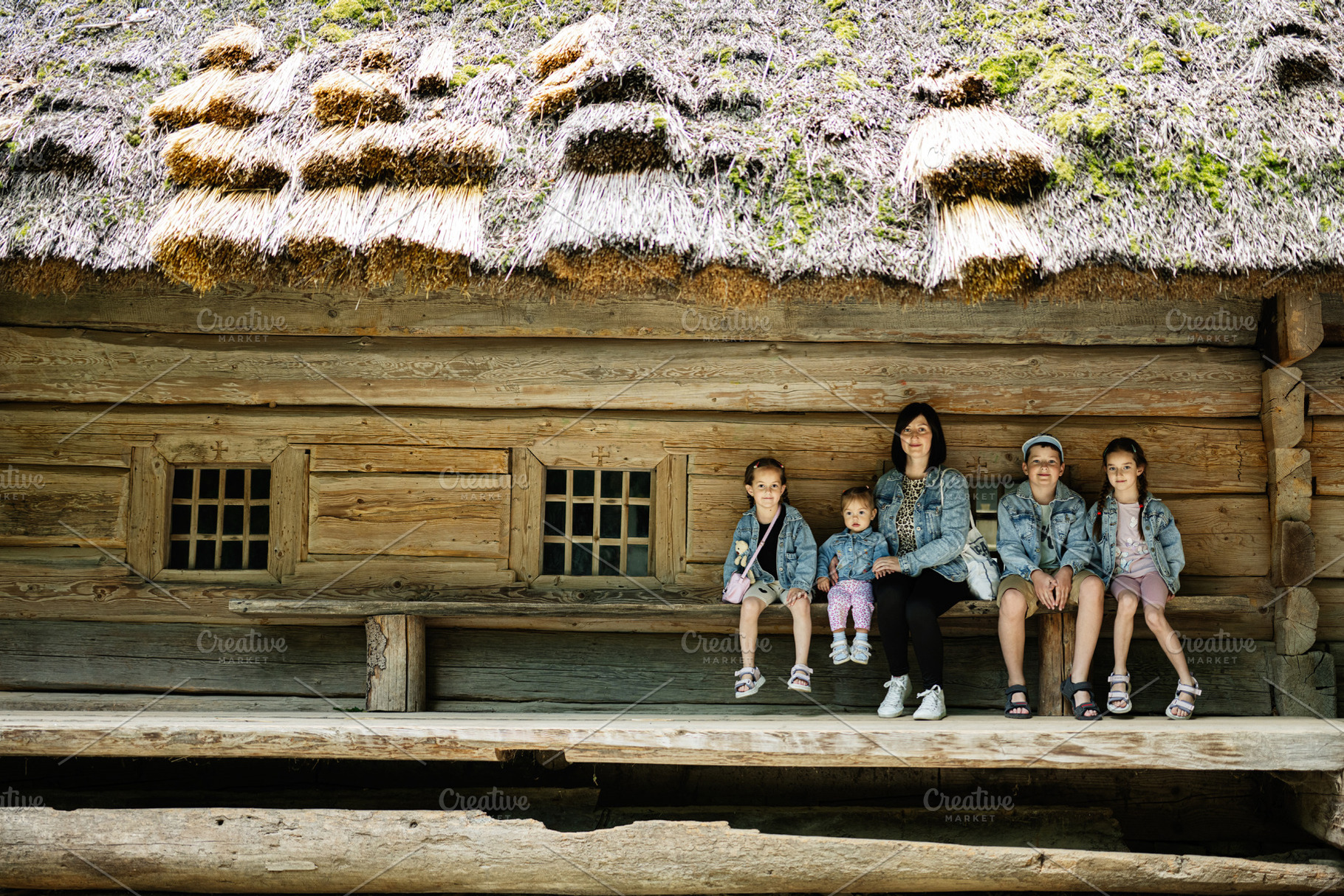 Family of five posing by a rustic wooden house with traditional thatched roof, a Person Photo by AS photostudio