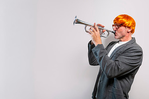 Man wearing orange wig playing trumpet, a Person Photo by karrastock
