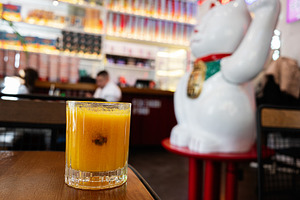 Orange beverage on a wooden table in a vibrant and colorful restaurant interior, a Photo by AS photostudio