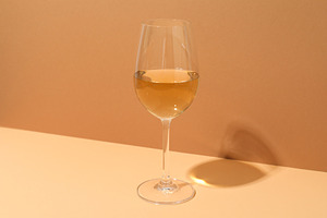 Glass of wine on beige table against light brown background, a Food & Drink Photo by AtlasStudio PRO