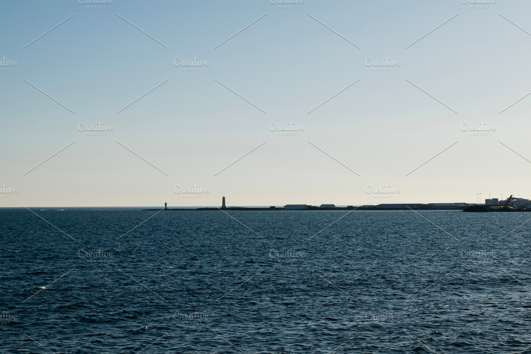 Coastal view of Akranes harbor with lighthouses and calm ocean under clear sky, a Photo by AS photostudio