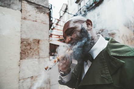 Black dapper man smoking outdoors, a Person Photo by SkyNext