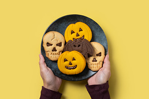 Hands holding plate with Halloween cookies shaped like pumpkins, skulls and bat, a Food & Drink Photo by etorres69