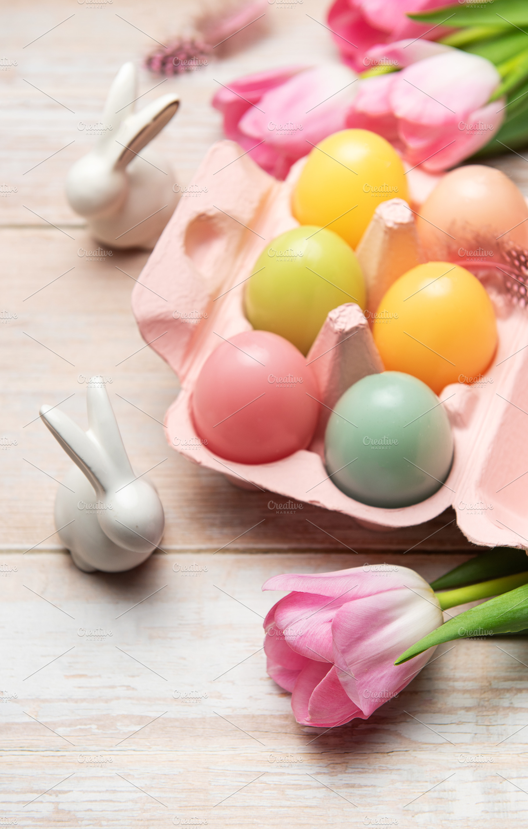 Easter eggs with ceramic bunnies and pink tulips decorating wood, a Holiday Photo by Olena Rudo