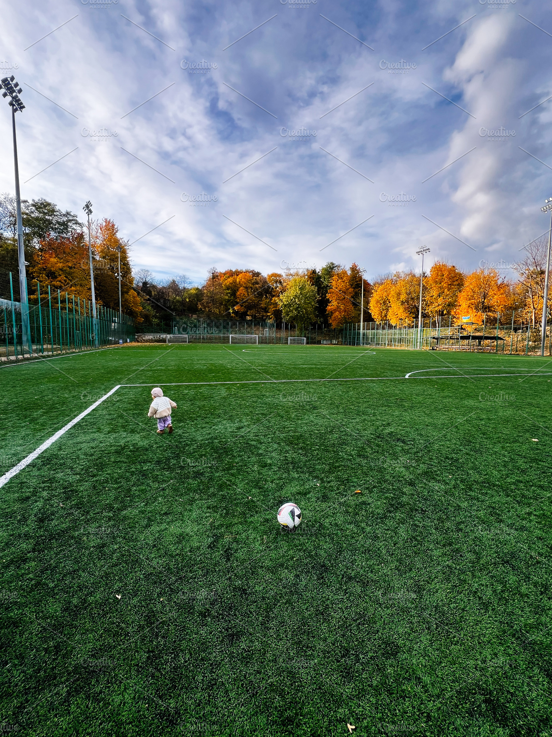 A small child on a green autumn soccer field with a ball under a bright sky, a Photo by AS photostudio