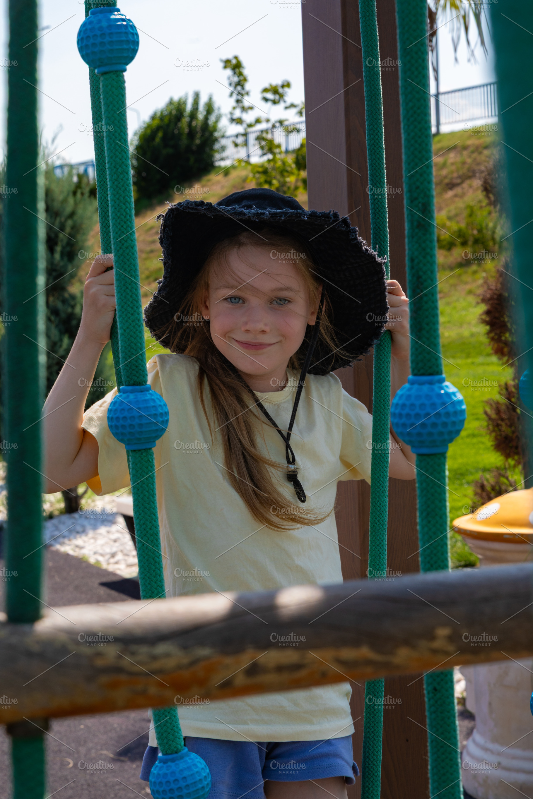 Cheerful young girl in a sun hat plays on outdoor playground ropes, enjoying a, a Person Photo by Ales Munt