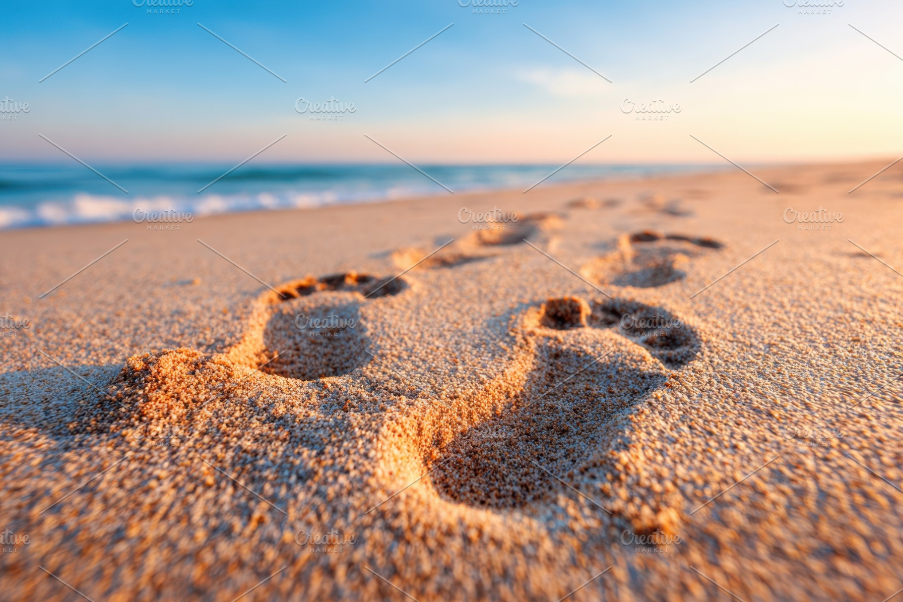 Footprints in sand on a beach at sunrise, a Background Photo by AlyaAnd