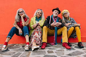 Carefree elderly friends sitting against a red wall, a Person Photo by Jacob Lund