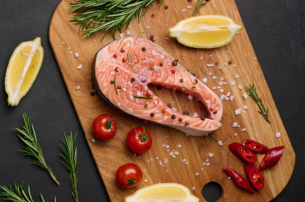 Raw salmon steak on a wooden cutting board, lemon slices, spices, a Food & Drink Photo by ndanko