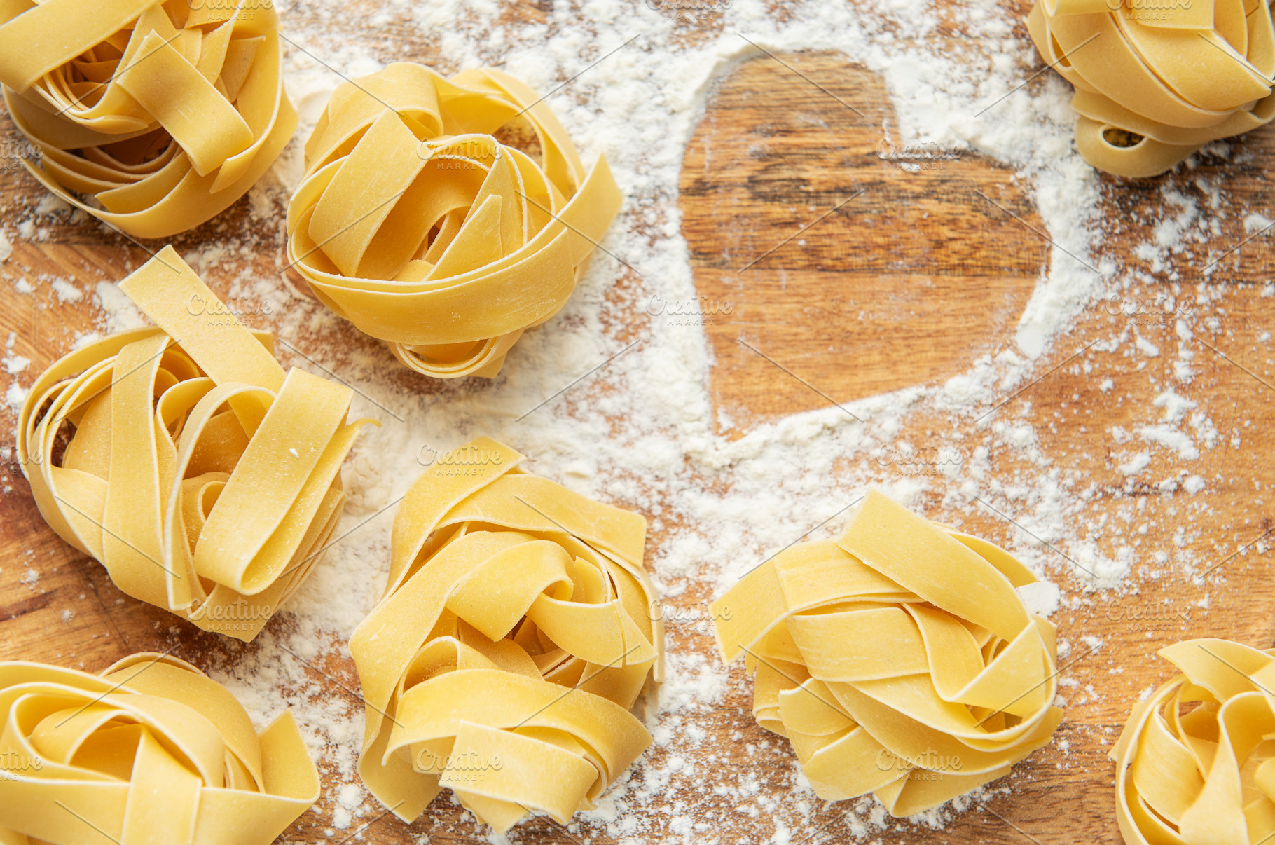 Uncooked tagliatelle pasta nests with heart of flour on wooden b, a Food & Drink Photo by Olena Rudo