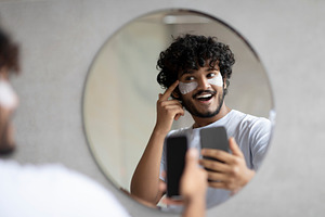 Excited indian man with eye patches taking photo on cellphone, looking and smil, a Person Photo by Prostock-Studio