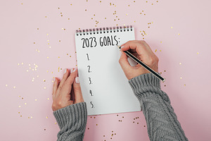 Woman's hand writing 2023 goals in note pad on pink background. Concept of New
