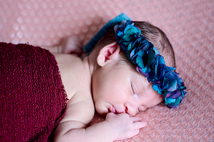 a naked newborn sleeping on a pink blanket and wearing a blue flower headband, a Photo by YossSabalet