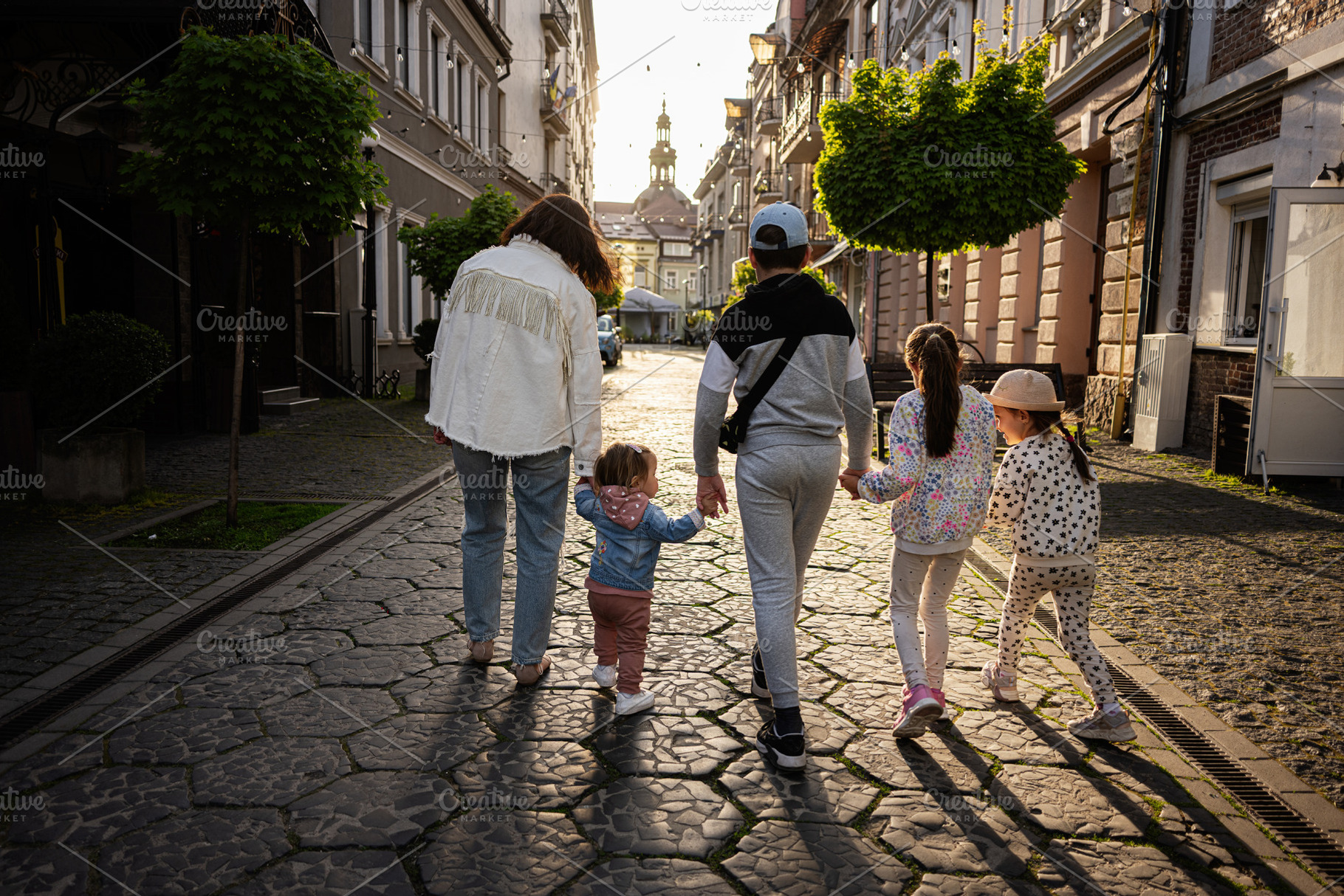 Family walking together down a charming street during sunset in a historic city, a Person Photo by AS photostudio