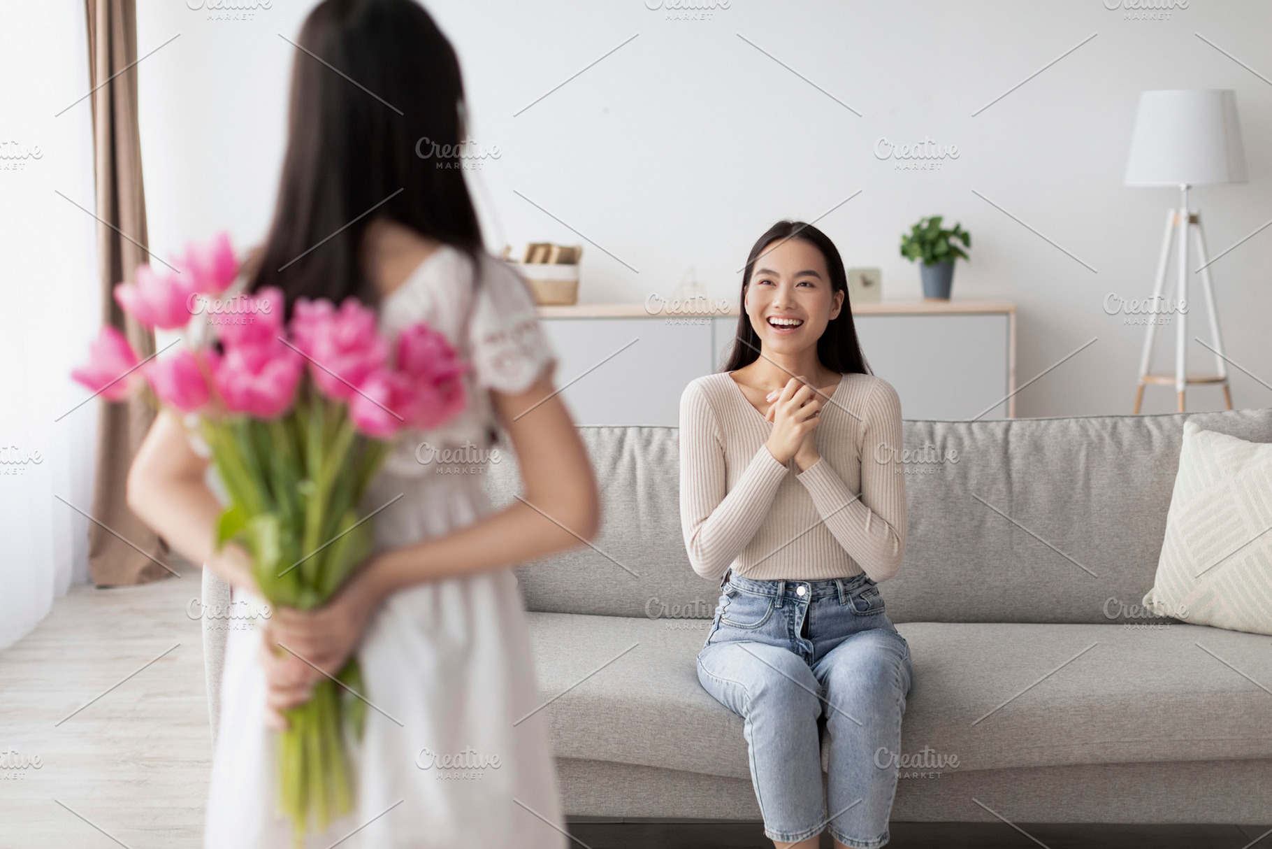 Little Asian girl holding bouquet of flowers behind back, making holiday surpri, a Photo by Prostock-Studio