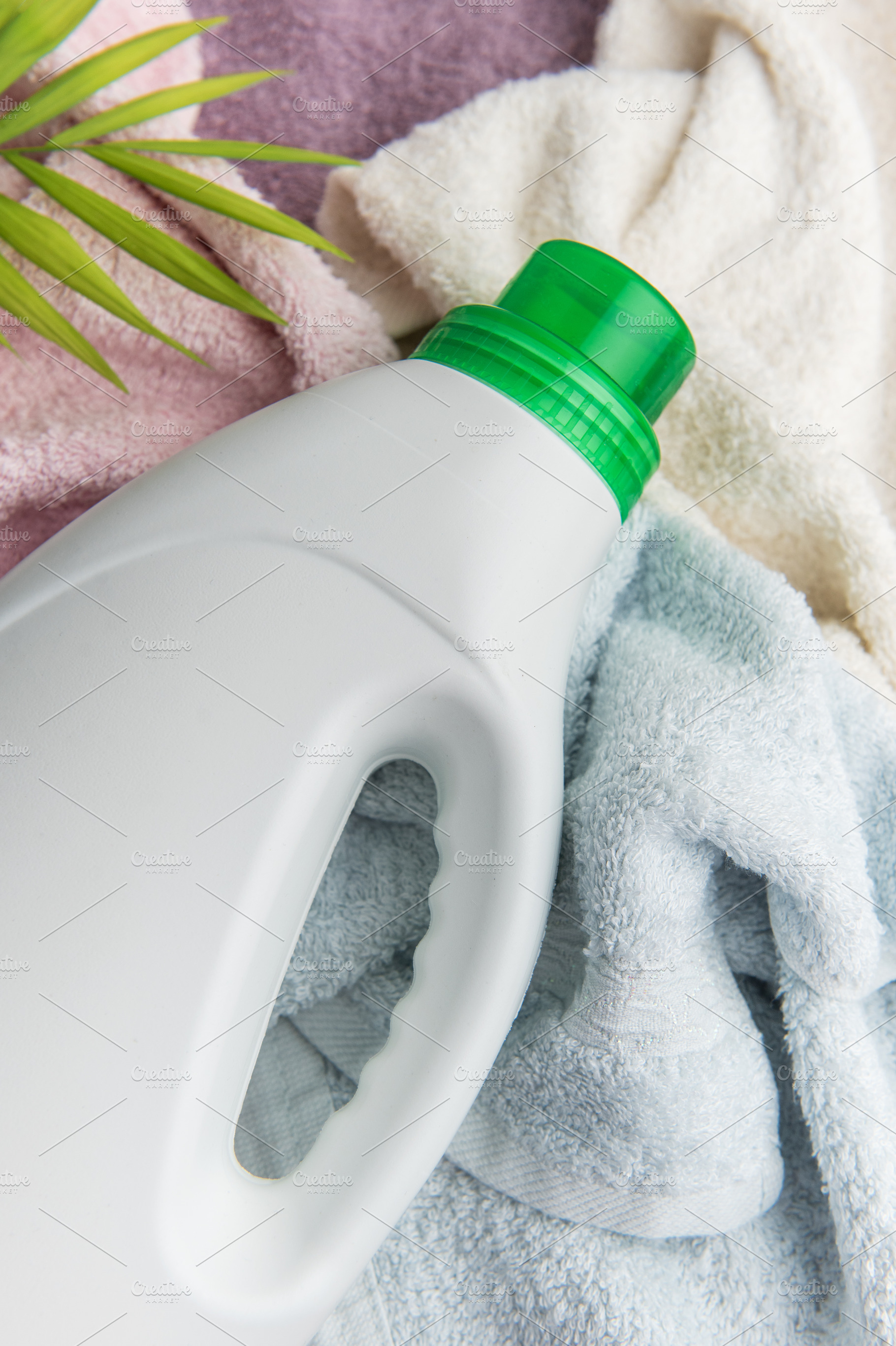 Laundry detergent bottle resting on clean towels and tropical le, an Industrial Photo by Olena Rudo
