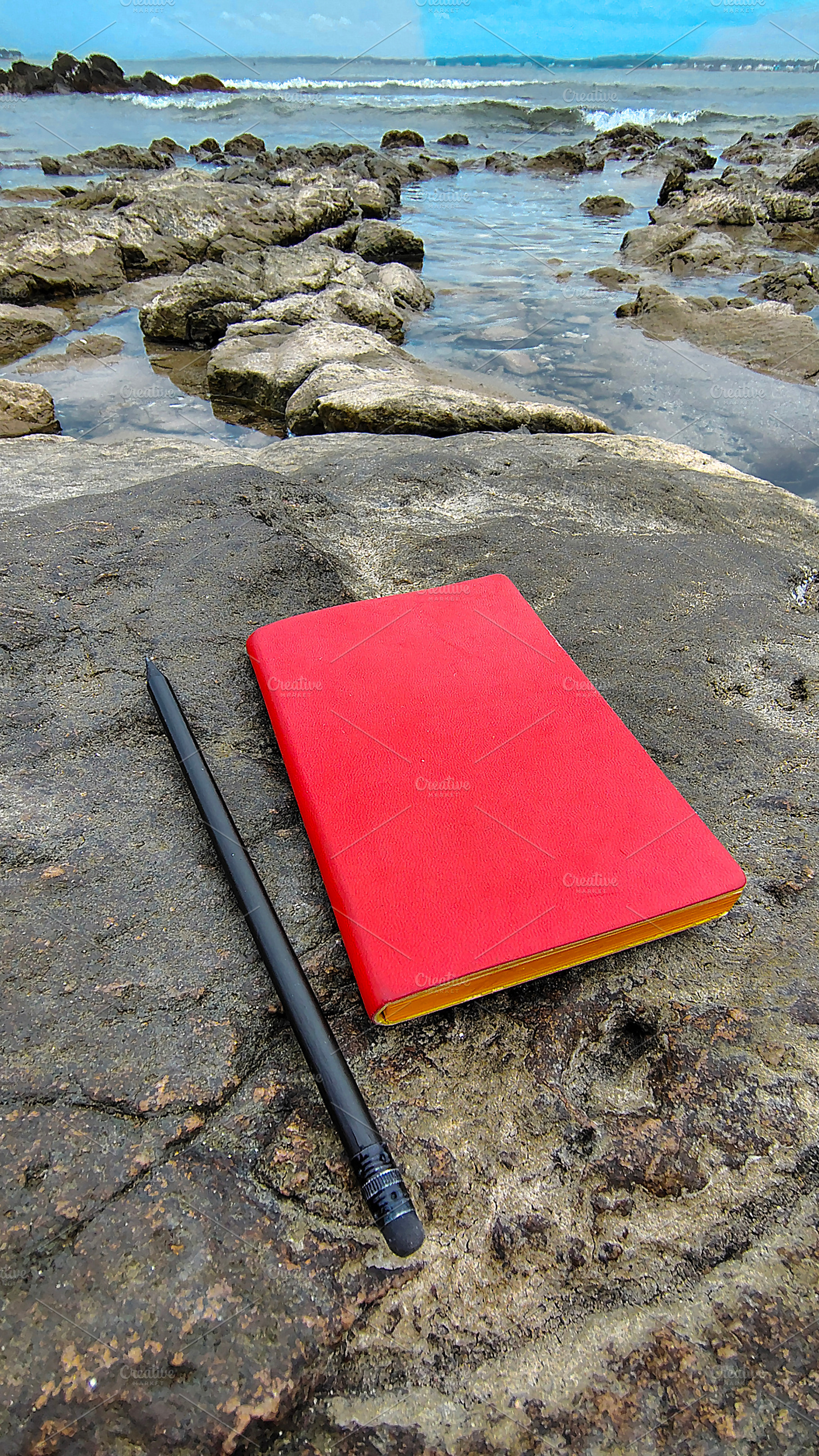 Notebook and a pencil rest on a rugged rock along a rocky beach,, a Sports & Recreation Photo by DanFLCreativo