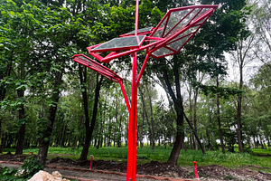 Red solar powered charging station in a park surrounded by greenery, a Photo by AS photostudio