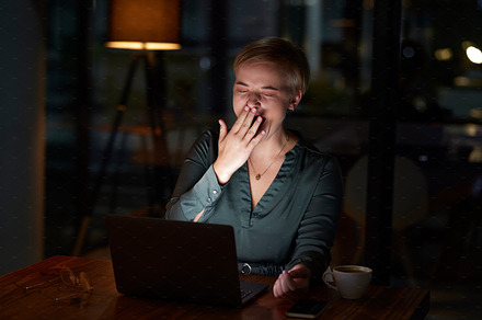 Tired, late and woman working on a laptop, yawning and feeling burnout in a dark office. Sleepy, overworked and employee with fatigue doing overtime for a project deadline at night on a computer, a Photo by Peopleimages.com